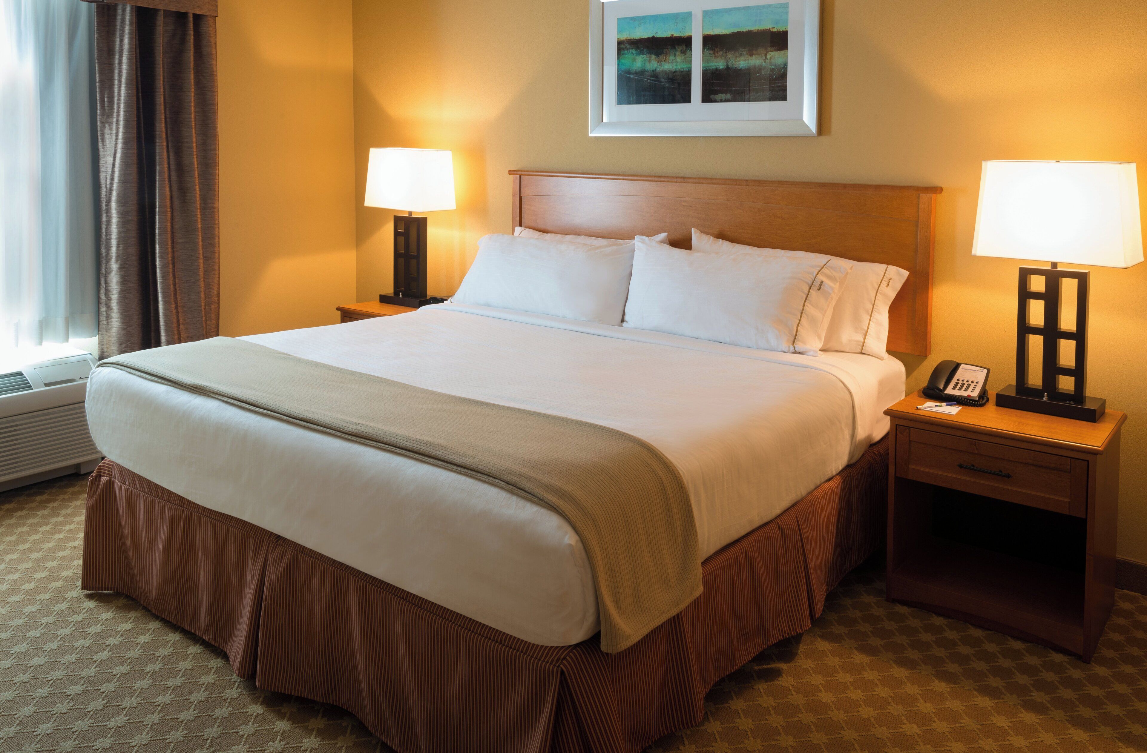 A hotel room with a large bed, two bedside tables with lamps, a framed picture on the wall, and a window with curtains.