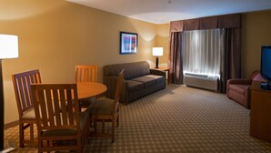 A hotel room with a sofa, two wooden chairs, a dining table, a TV, a lamp, and a window with curtains. - Holiday Inn Express & Suites Chicago West-Roselle by IHG (Roselle)