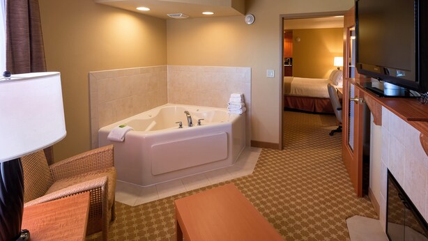 A hotel bathroom with a large bathtub, a television, and a separate bedroom visible through an open door. - Holiday Inn Express & Suites Chicago West-Roselle by IHG (Roselle)