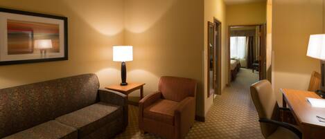 A hotel room with a sofa, armchair, desk, and lamps.