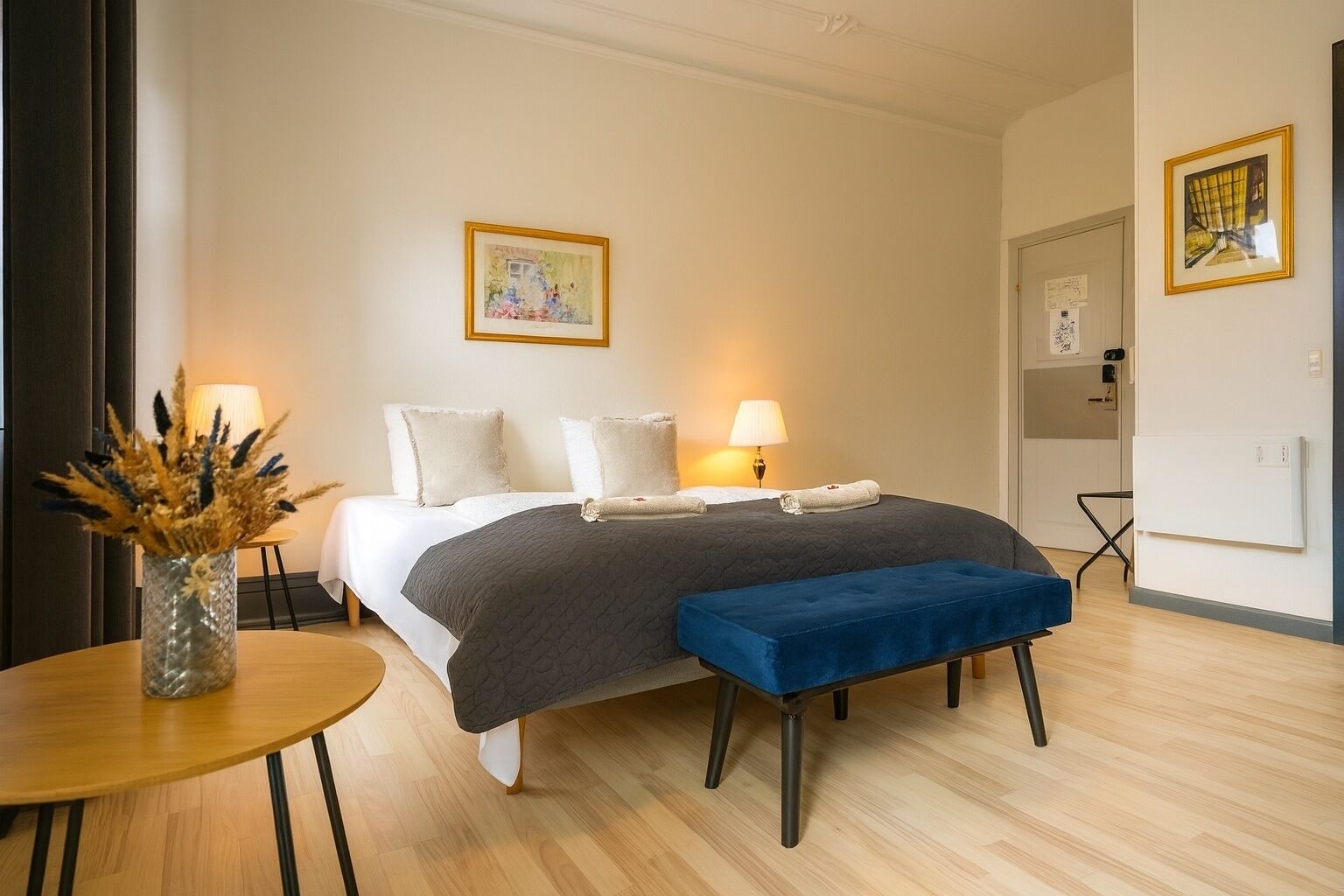 Un dormitorio moderno con cama, lámparas de noche, una mesita con un florero y un banco.