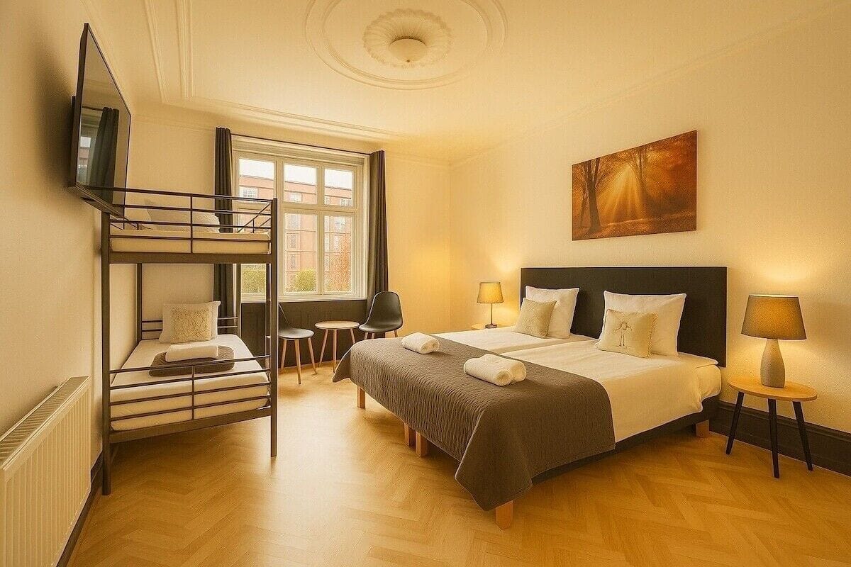A hotel room with a bunk bed, a single bed, a TV, a painting, and two bedside lamps.