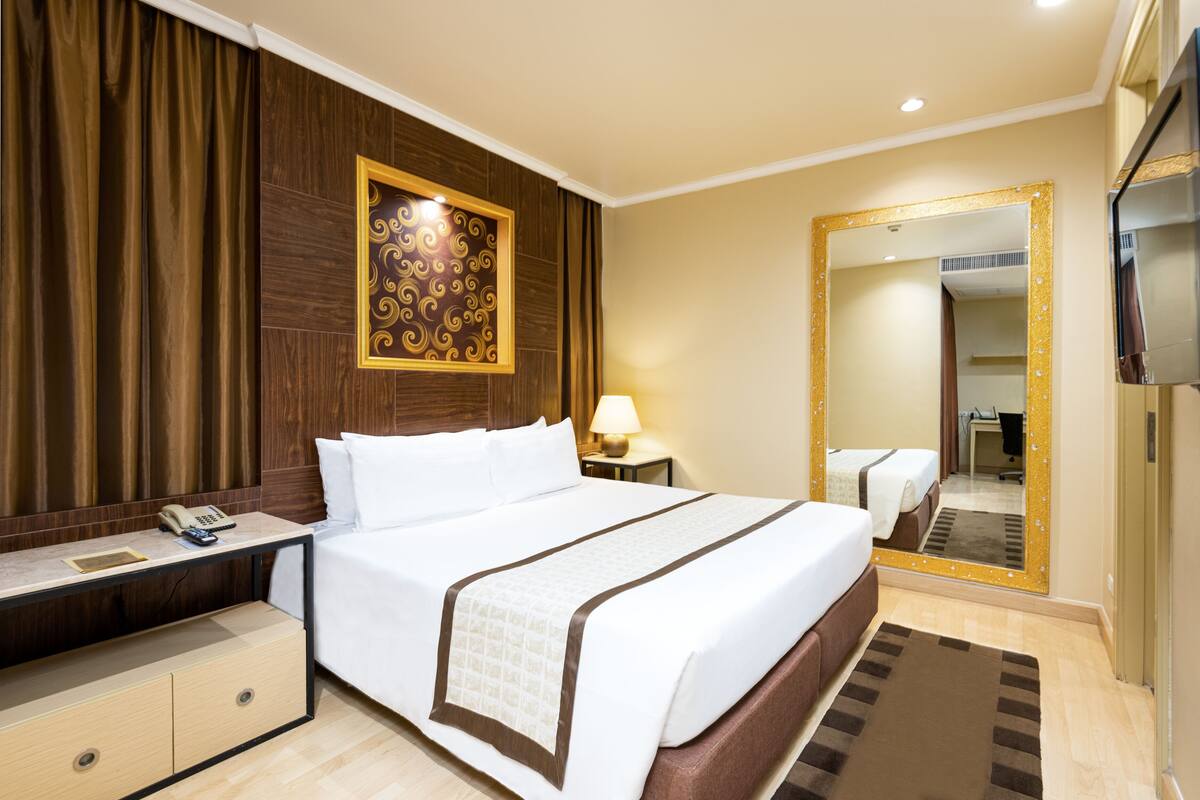 A hotel room with a large bed, a bedside table with a lamp, a mirror, and a TV.