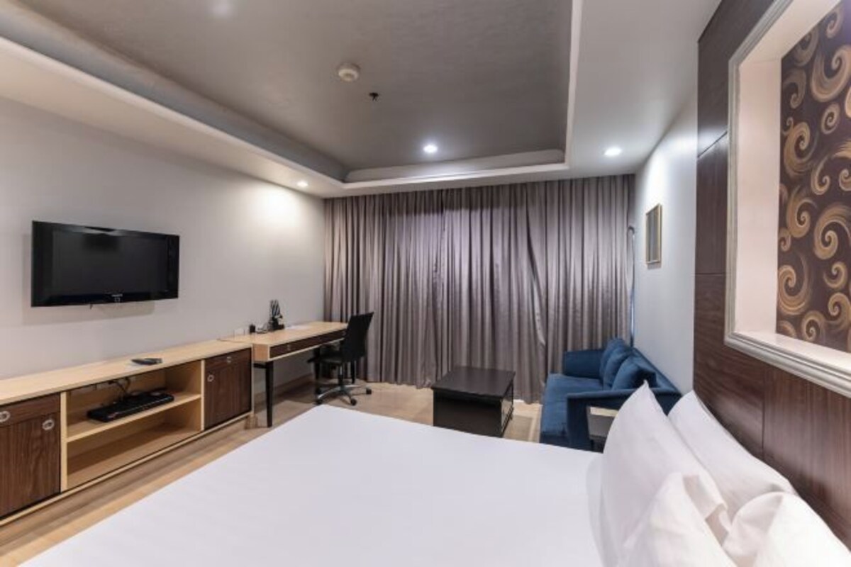 A hotel room with a bed, desk, chair, TV, and curtains.