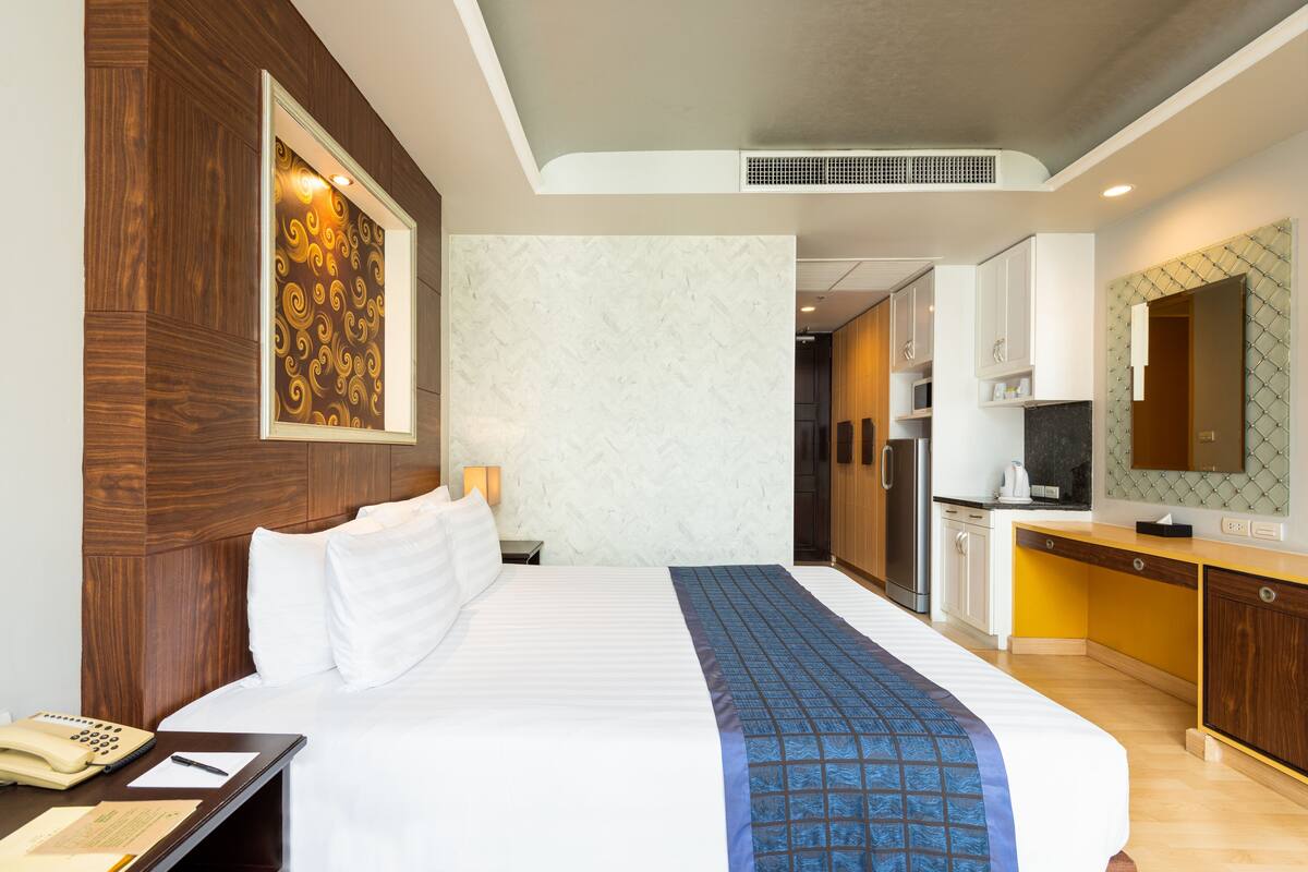 A hotel room with a large bed, a desk with a telephone and papers, a microwave, and a kitchenette.