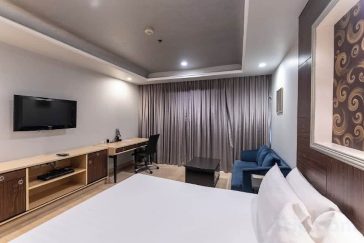 A hotel room with a bed, a desk, a chair, a television, and a curtain.