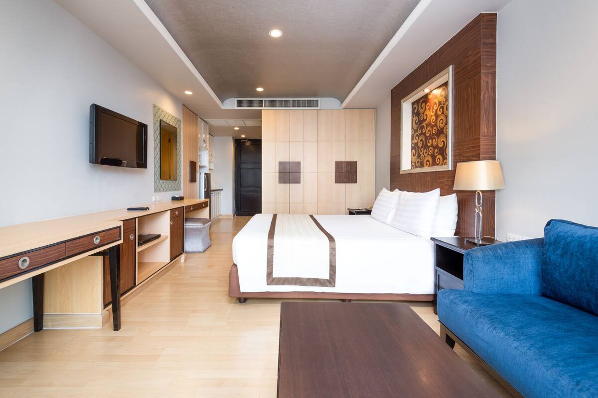 A hotel room with a bed, a desk, a TV, a sofa, and a painting on the wall.