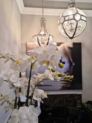 A room with a large painting of a boat on water, a vase of white orchids, and two hanging light fixtures. - Villahotel Rheinblick (Cologne)
