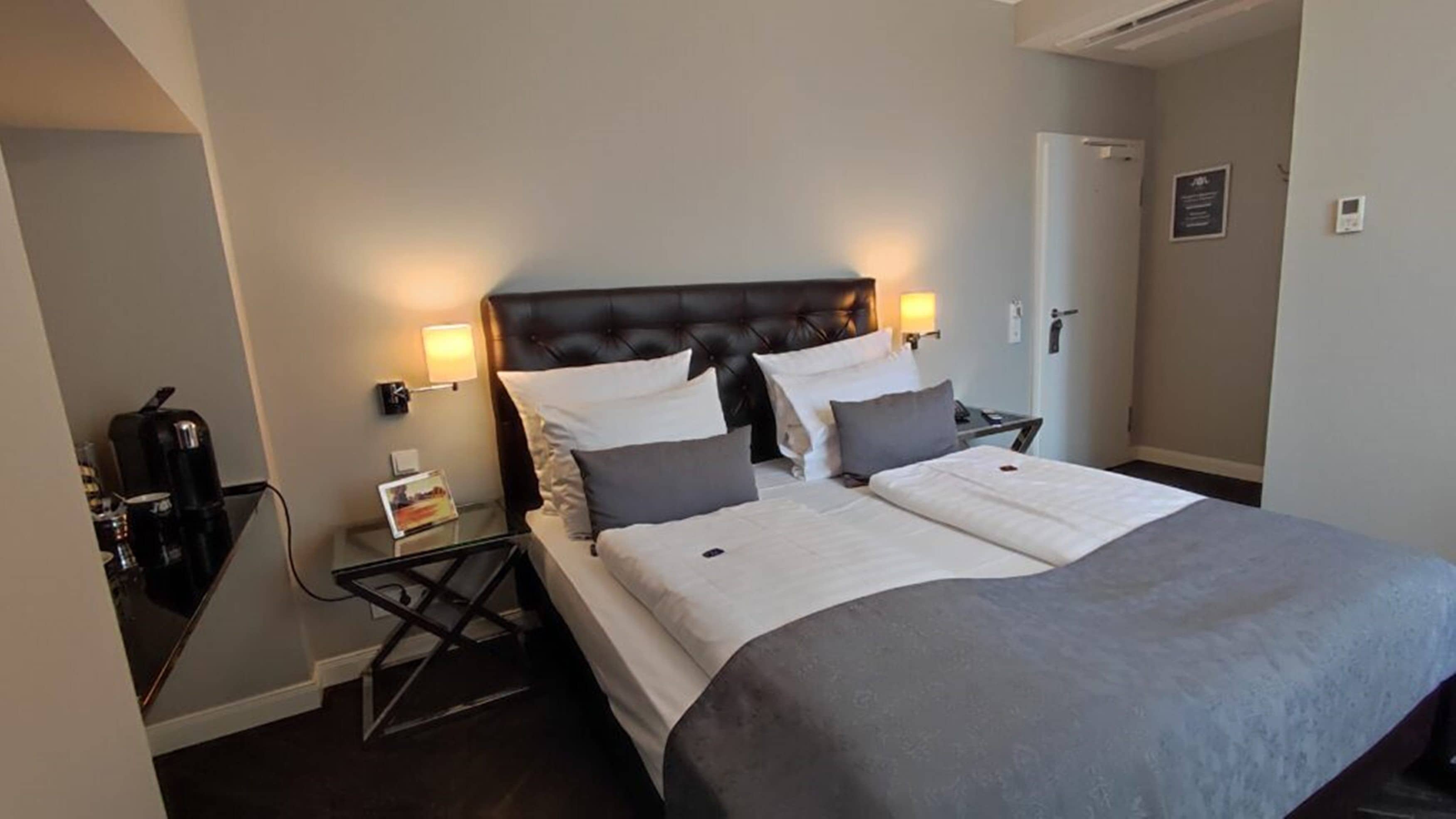 Une chambre d’hôtel avec un lit double, des tables de chevet, une machine à café et une porte.