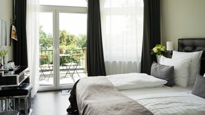 A hotel room with a bed, a desk, a chair, a balcony with a table and chairs, and a window with curtains. - Villahotel Rheinblick (Cologne)