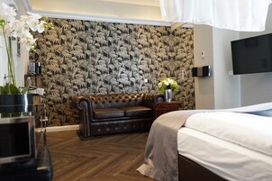 Ein Schlafzimmer mit einem Bett, einem Ledersofa, einem Fernseher und einer Wand mit Blätermotiv.