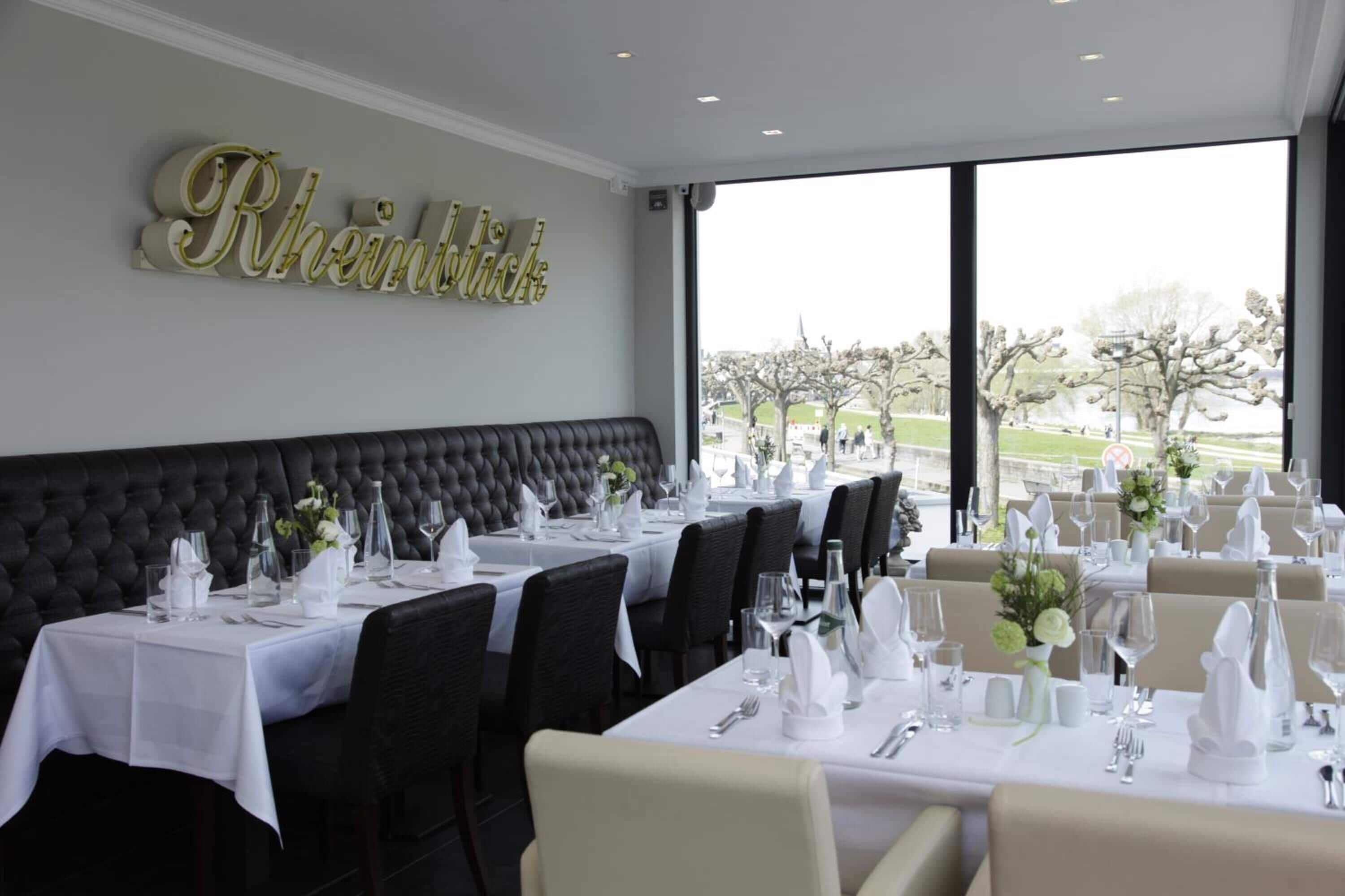 Een restaurant met een zwarte beklede bank, witte tafellakens en een groot bord aan de muur.