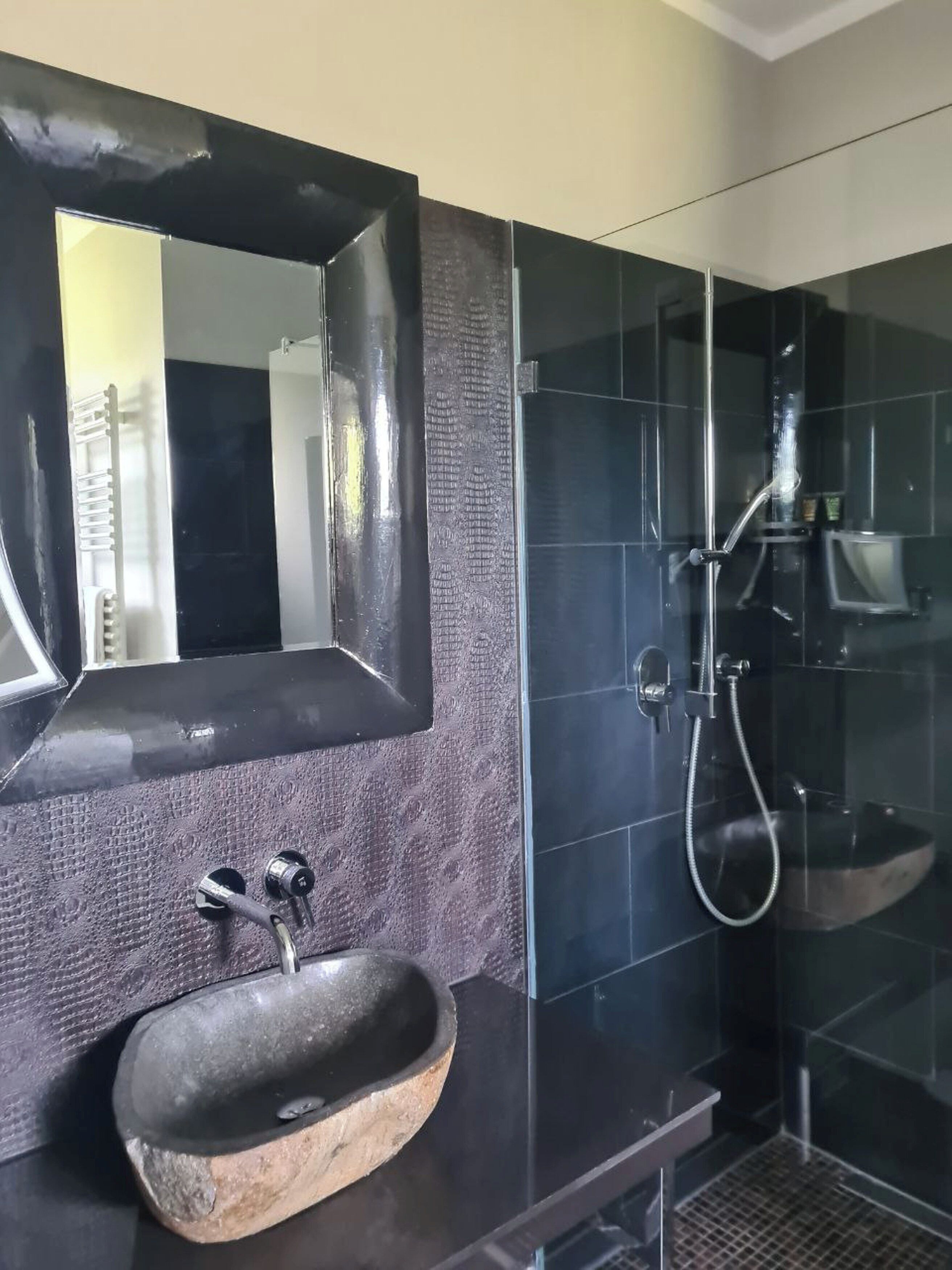 Un baño moderno con un espejo grande, un lavabo de piedra y una ducha con mampara de vidrio.