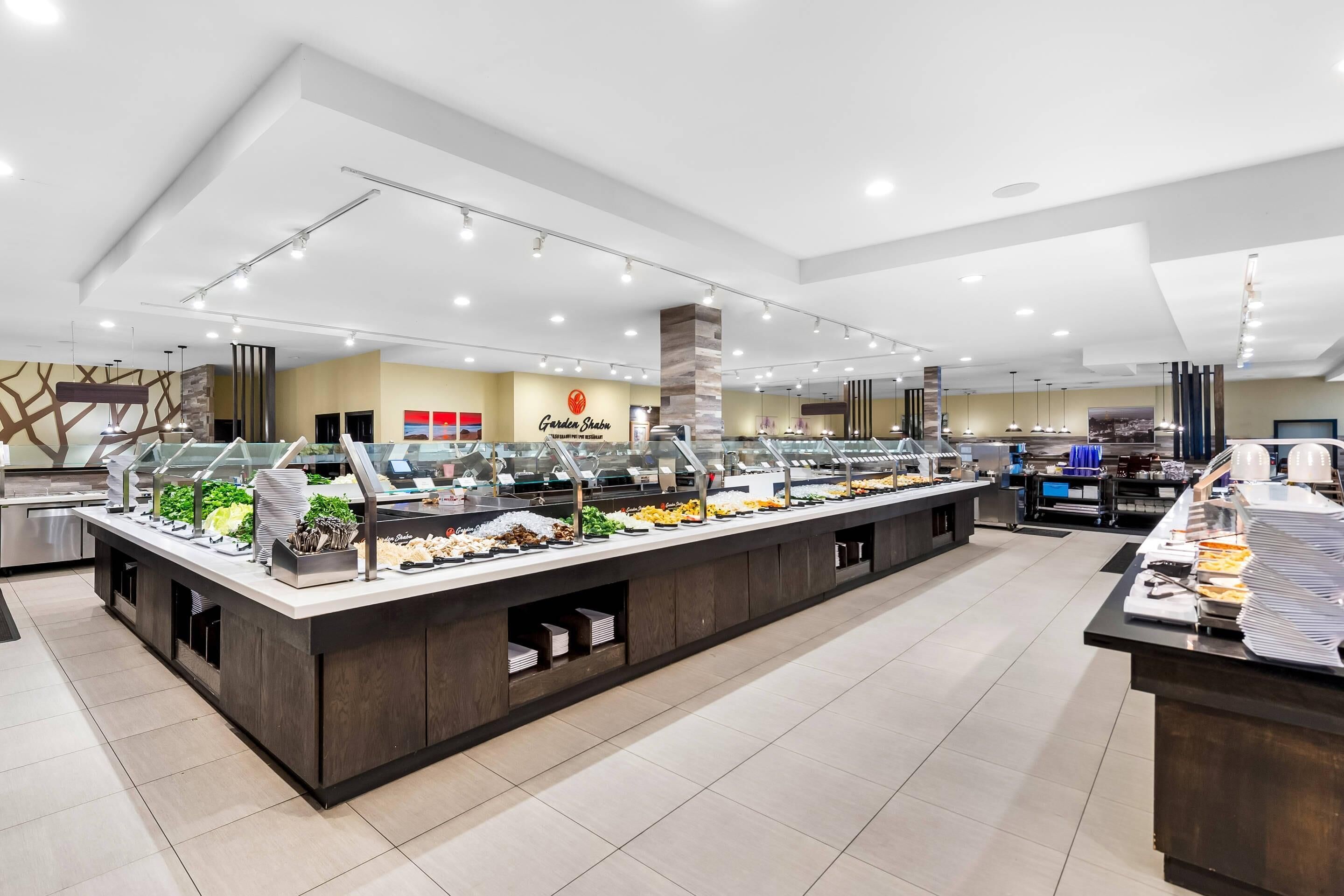 Zona de buffet con varias estaciones de comida, un logotipo en la pared y un diseño interior moderno.