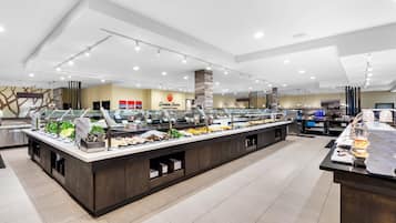 Zona de buffet con varias estaciones de comida, un logotipo en la pared y un diseño interior moderno.