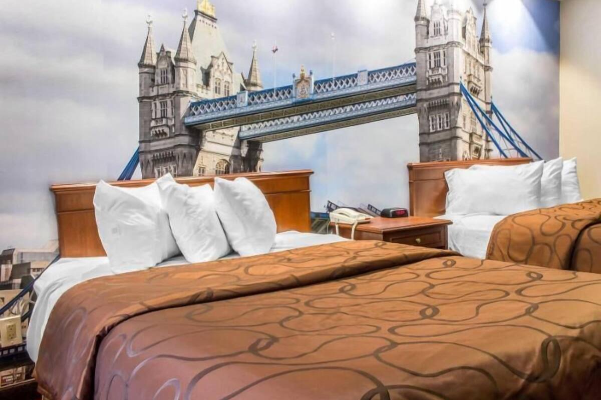 A hotel room with a large bed, a wooden headboard, a nightstand, and a wall mural of a bridge.
