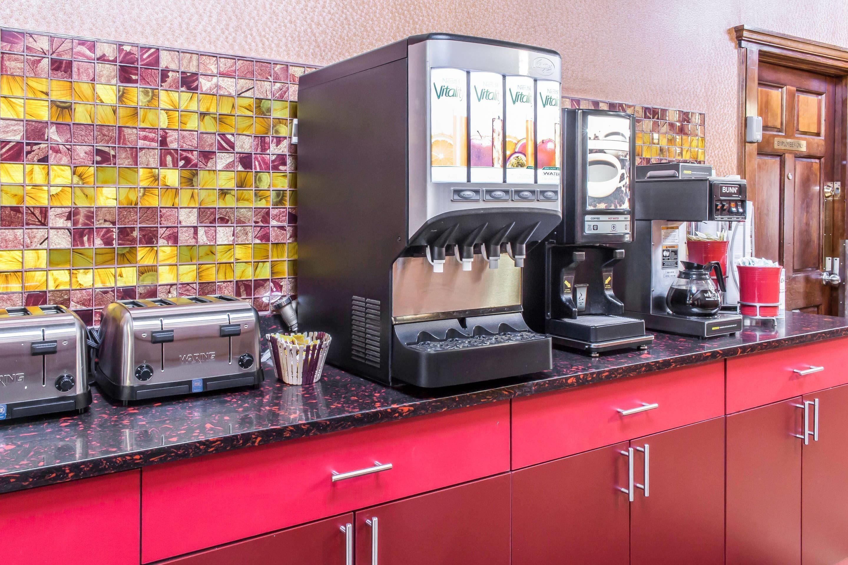 A coffee station with a water cooler, coffee machine, and two toasters on a red countertop.