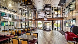 A spacious indoor area with multiple dining tables and chairs, a central open space, and a view through glass doors. - Rodeway Inn Capri (Little Ferry)