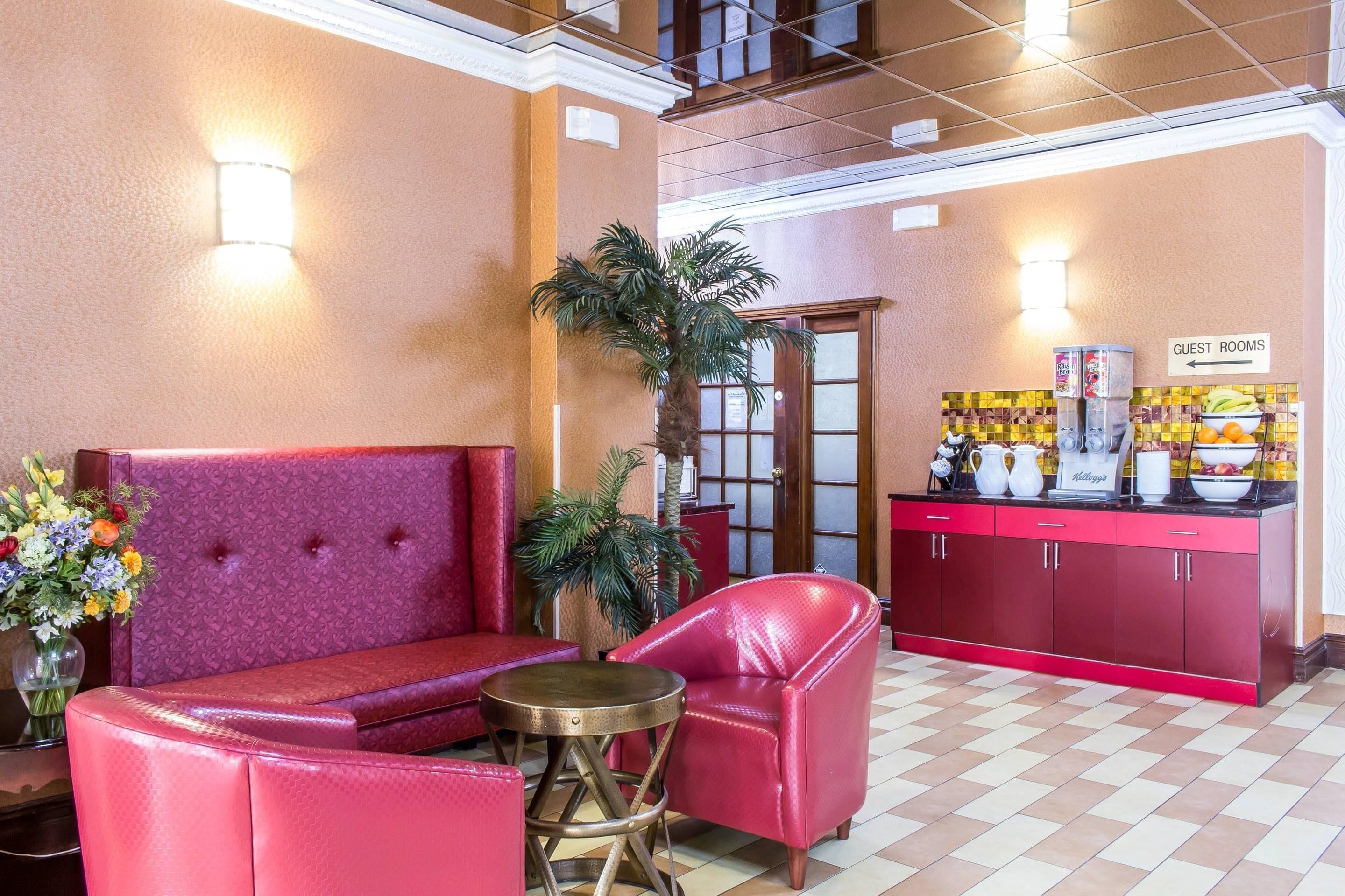 A lobby with a red sofa, a red armchair, a small round table, a potted plant, and a counter with a sign indicating guest rooms.