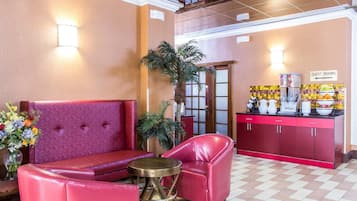 A lobby with a red sofa, a red armchair, a small round table, a potted plant, and a counter with a sign indicating guest rooms.