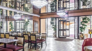 A spacious indoor area with multiple tables and chairs, large windows, and a central open space. - Rodeway Inn Capri (Little Ferry)