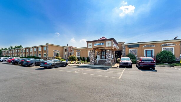 A hotel with a parking lot, a central entrance, and a clear sky. - Rodeway Inn Capri (Little Ferry)
