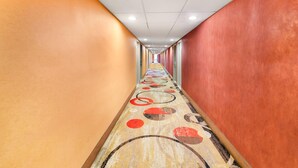 A long corridor with patterned carpet, white ceiling, and red walls. - Rodeway Inn Capri (Little Ferry)