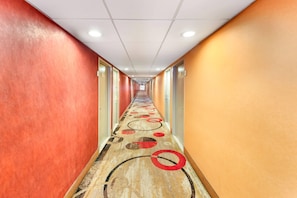A hotel corridor with a patterned carpet, red and yellow walls, and doors on both sides.