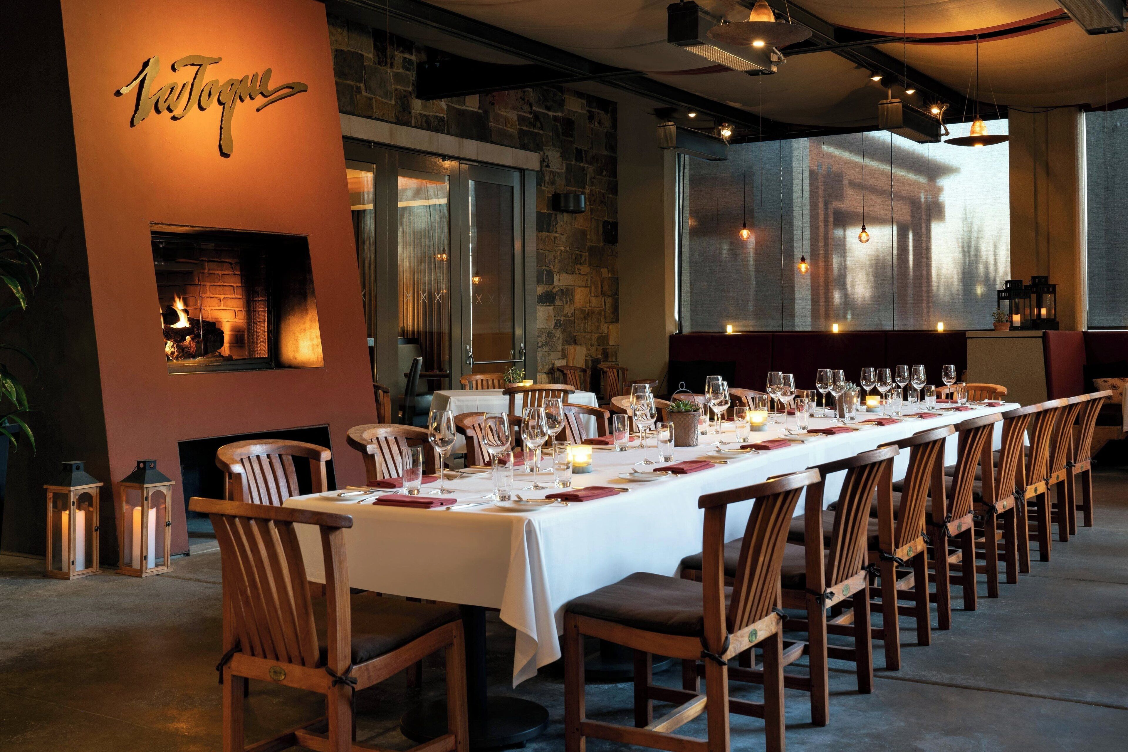 A long dining table set with chairs, a fireplace, and a stone wall.