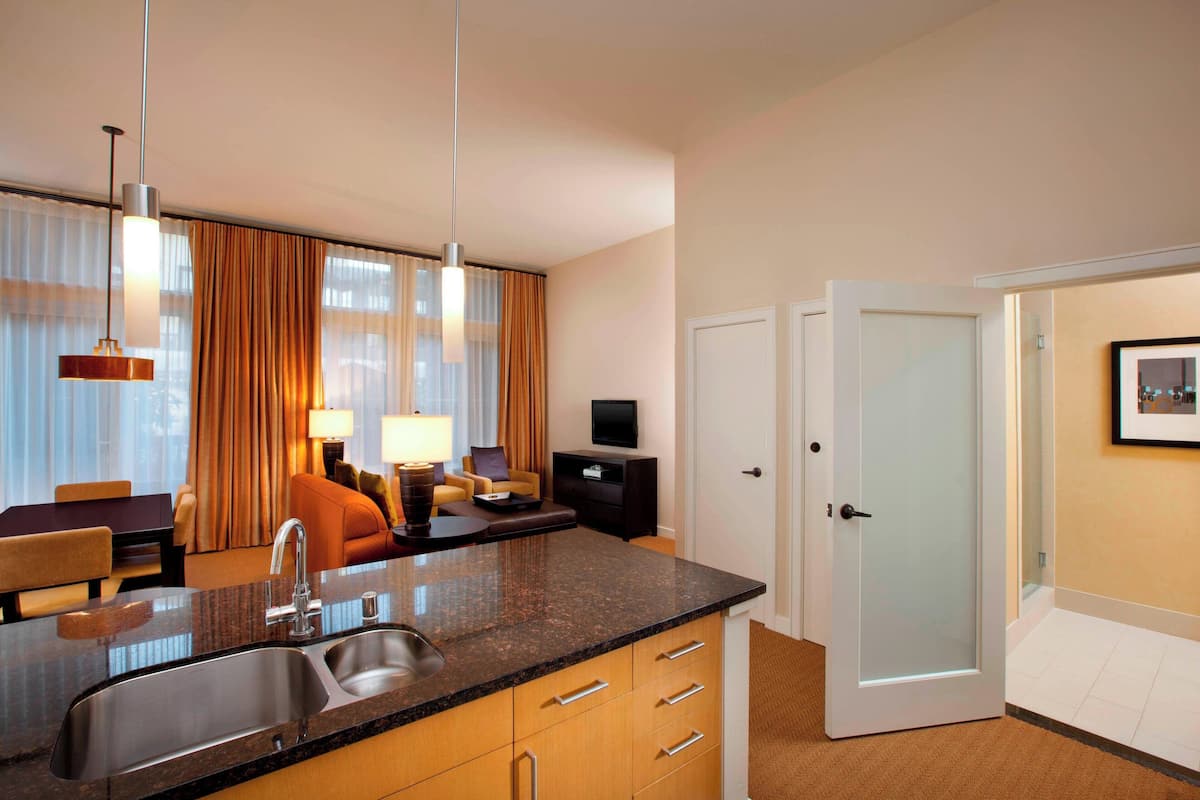 A modern hotel room with a kitchen area, a dining area, and a living space.