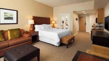 A hotel room with a bed, a sofa, a coffee table, a TV, and a kitchen area.