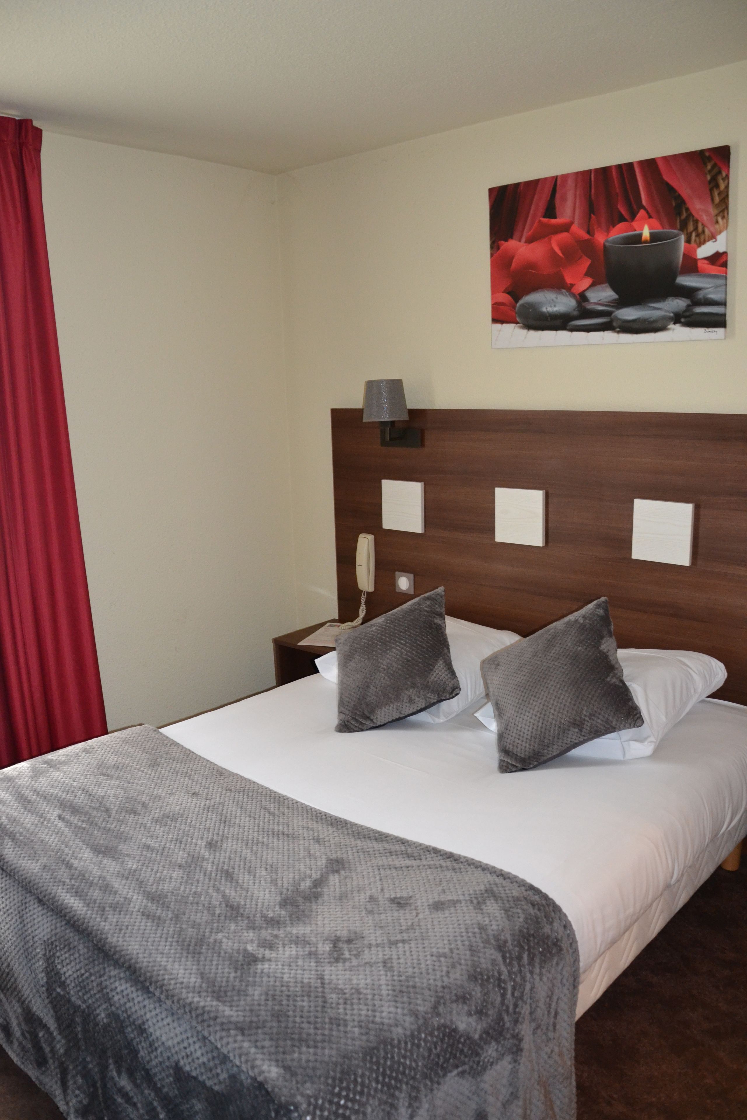 A hotel room with a bed, a nightstand, a lamp, and a painting on the wall.