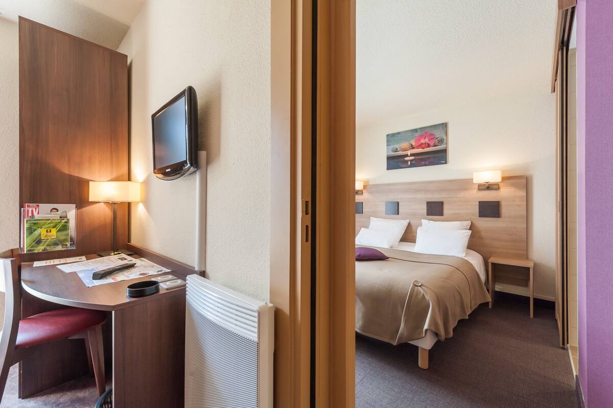 A hotel room with a bed, bedside table, lamp, and a desk with a chair.