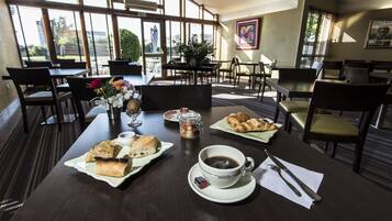 Un comedor con mesas dispuestas para el desayuno, incluyendo cruasanes, pasteles y café.