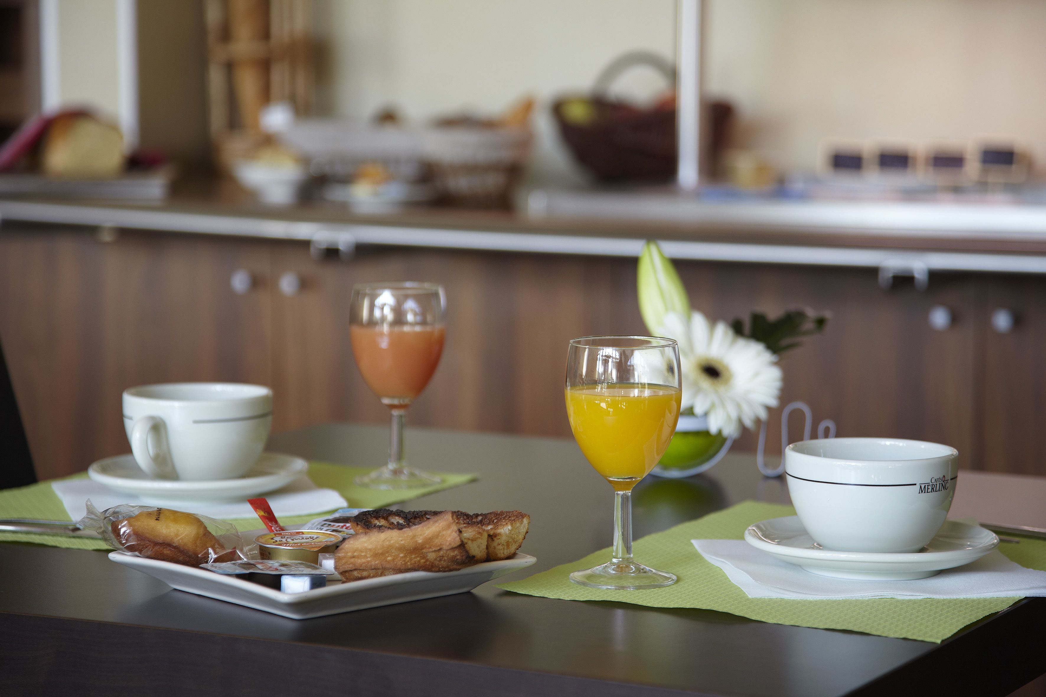 Une table dressée pour le petit-déjeuner, avec une assiette de nourriture, un verre de jus d’orange et une tasse de café.