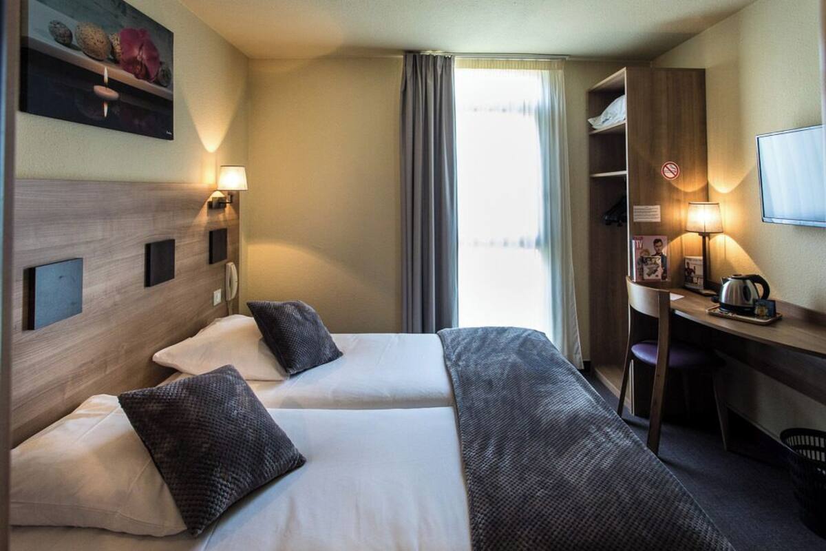 A hotel room with two beds, a desk with a chair, a television, and a window with curtains.