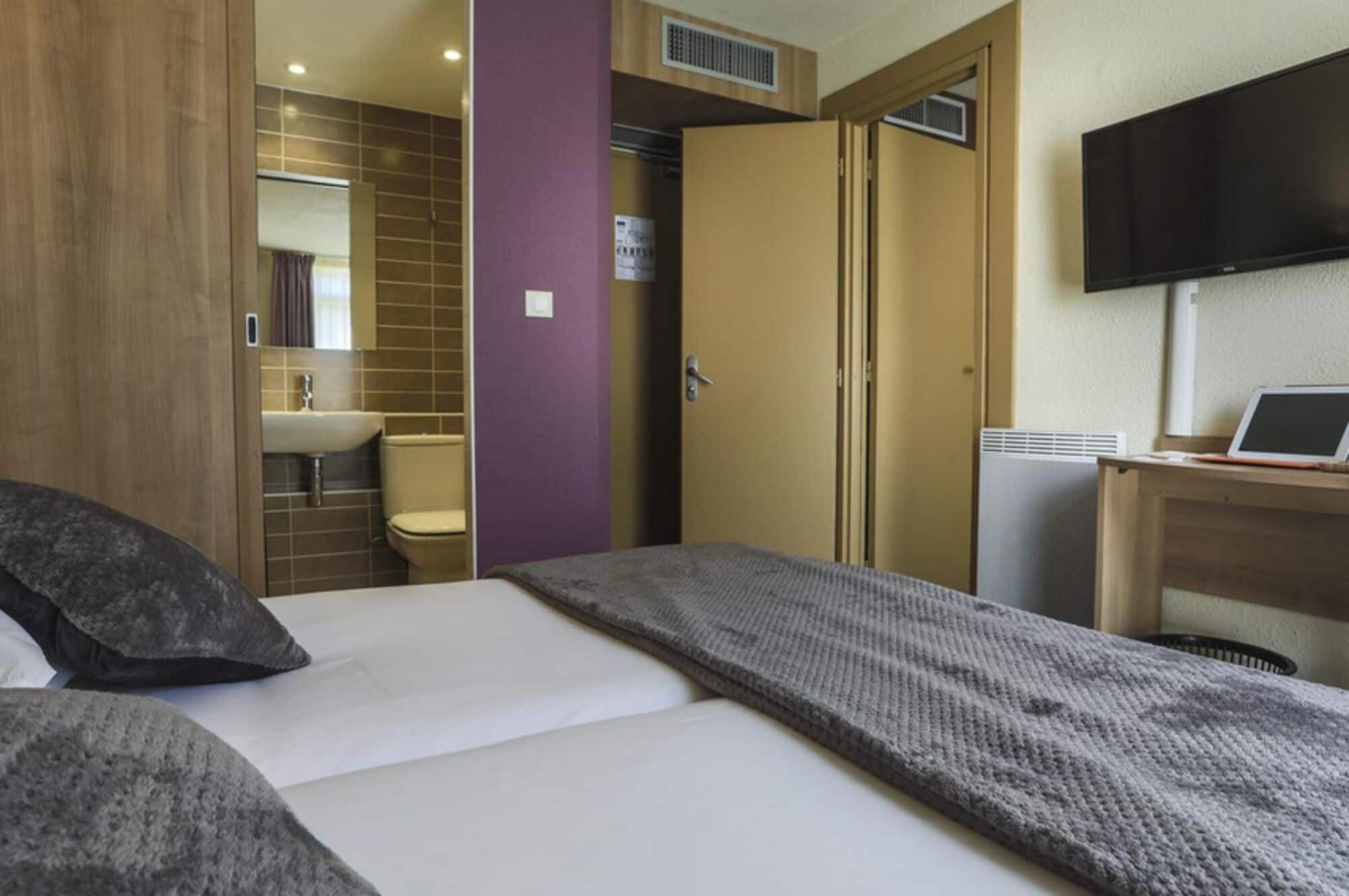 A hotel room with a bed, a bathroom, a TV, and a desk with a laptop.