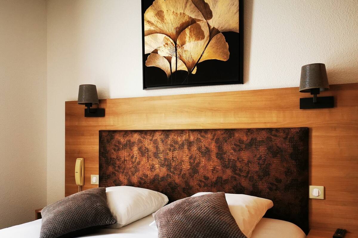 A hotel room with a wooden headboard, two bedside lamps, a telephone, and a large floral artwork above the bed.