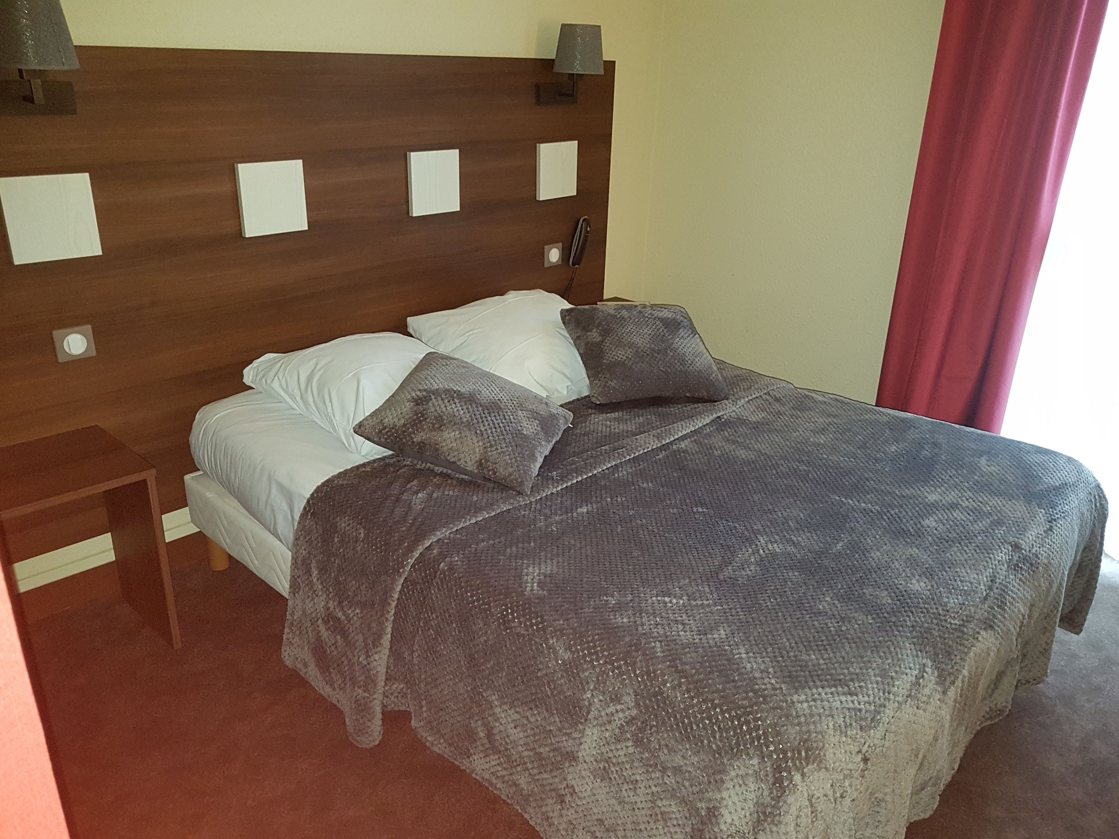Una cama con cabecera de madera, almohadas blancas y grises, y una manta gris.