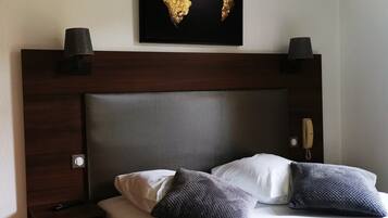 Una habitación de hotel con cabecera de madera, cama con ropa de cama blanca y gris oscuro, dos lámparas de noche y un mapa mundial enmarcado en la pared.