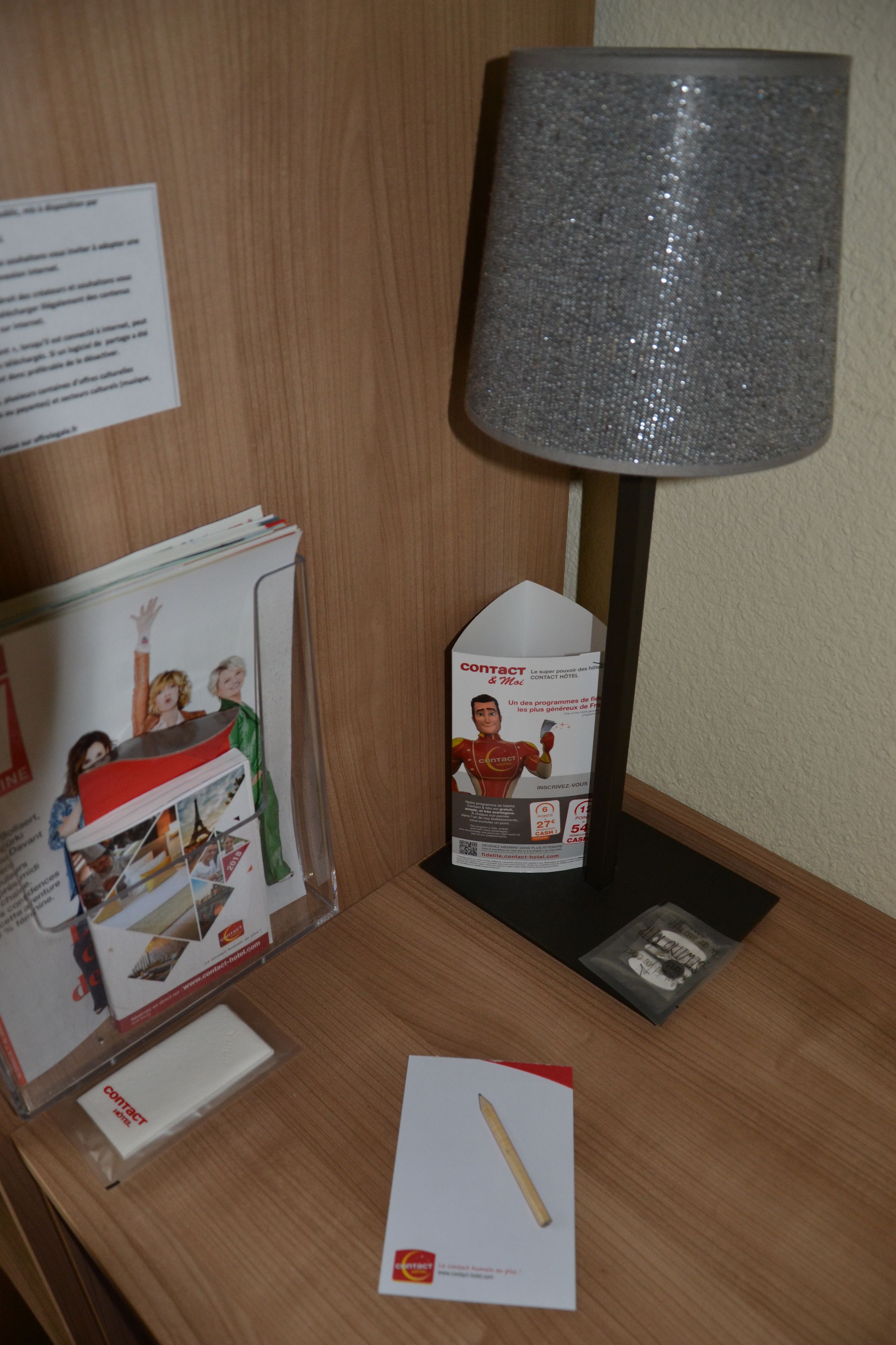 A hotel reception desk with a lamp, brochures, and a pen.