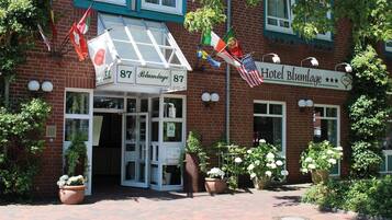A hotel entrance with a sign reading "Hotel Blümlage 87" and multiple flags, including the Swiss flag.