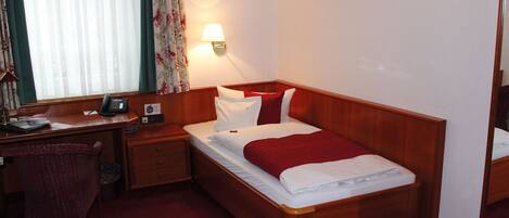 A hotel room with a wooden bed, a desk with a telephone, a chair, and a nightstand.