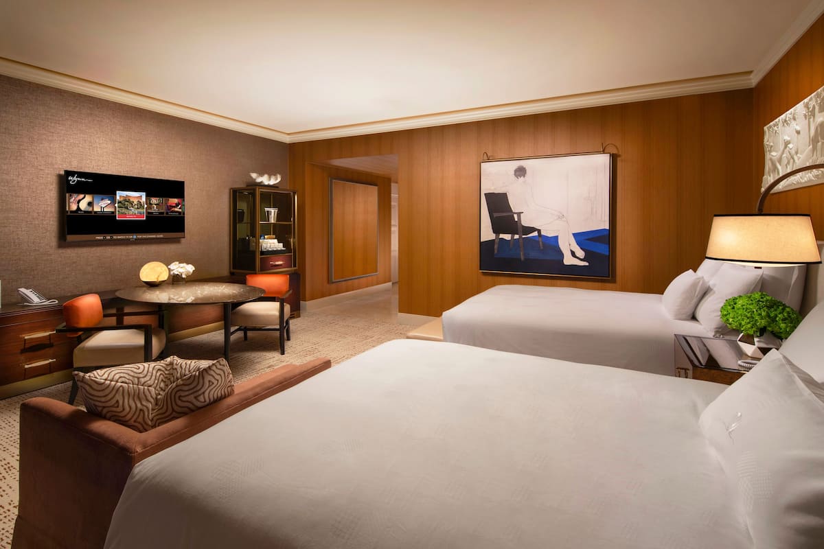 A hotel room with two beds, a TV, a desk with a chair, a small table, and a cabinet.