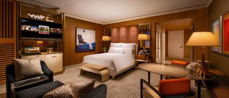 A hotel room with a large bed, a desk with a computer, a TV, and a seating area with chairs.