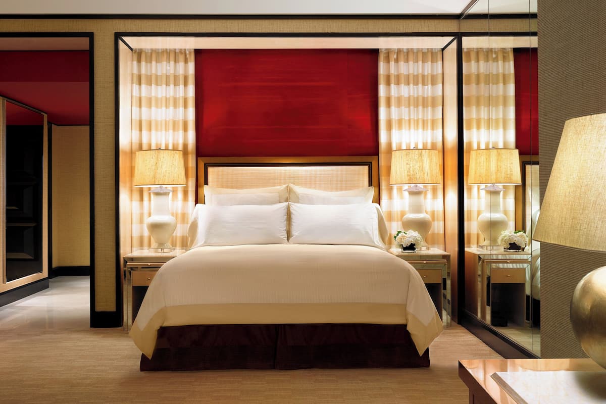 A hotel room with a large bed, two bedside tables with lamps, a mirror, and a wooden floor.