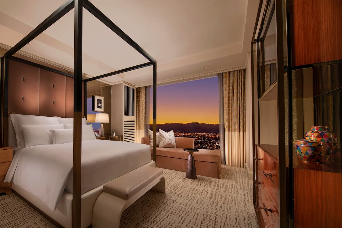 A four-poster bed with a city view, a sofa, a nightstand, and a lamp.
