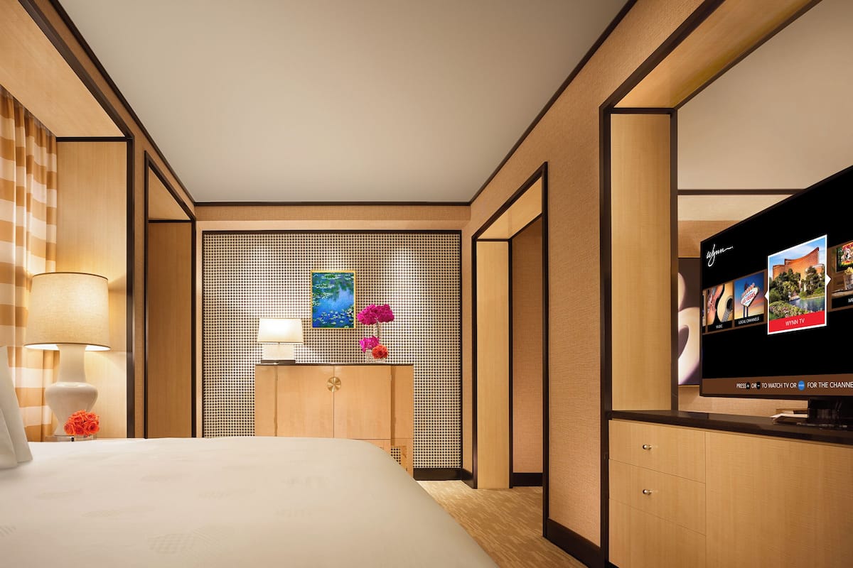 A hotel room with a bed, a TV, a wall-mounted picture, and a wooden cabinet.