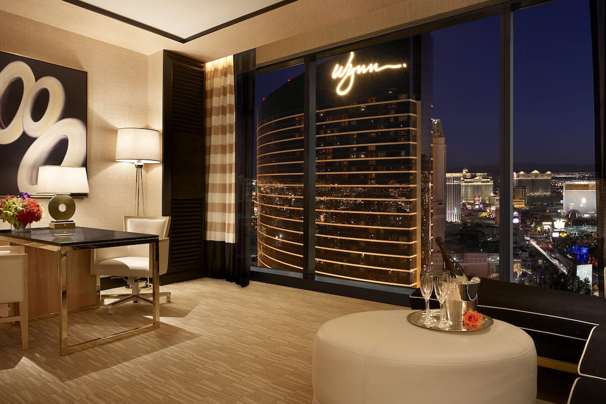A modern hotel room with a large window offering a view of a cityscape at night.