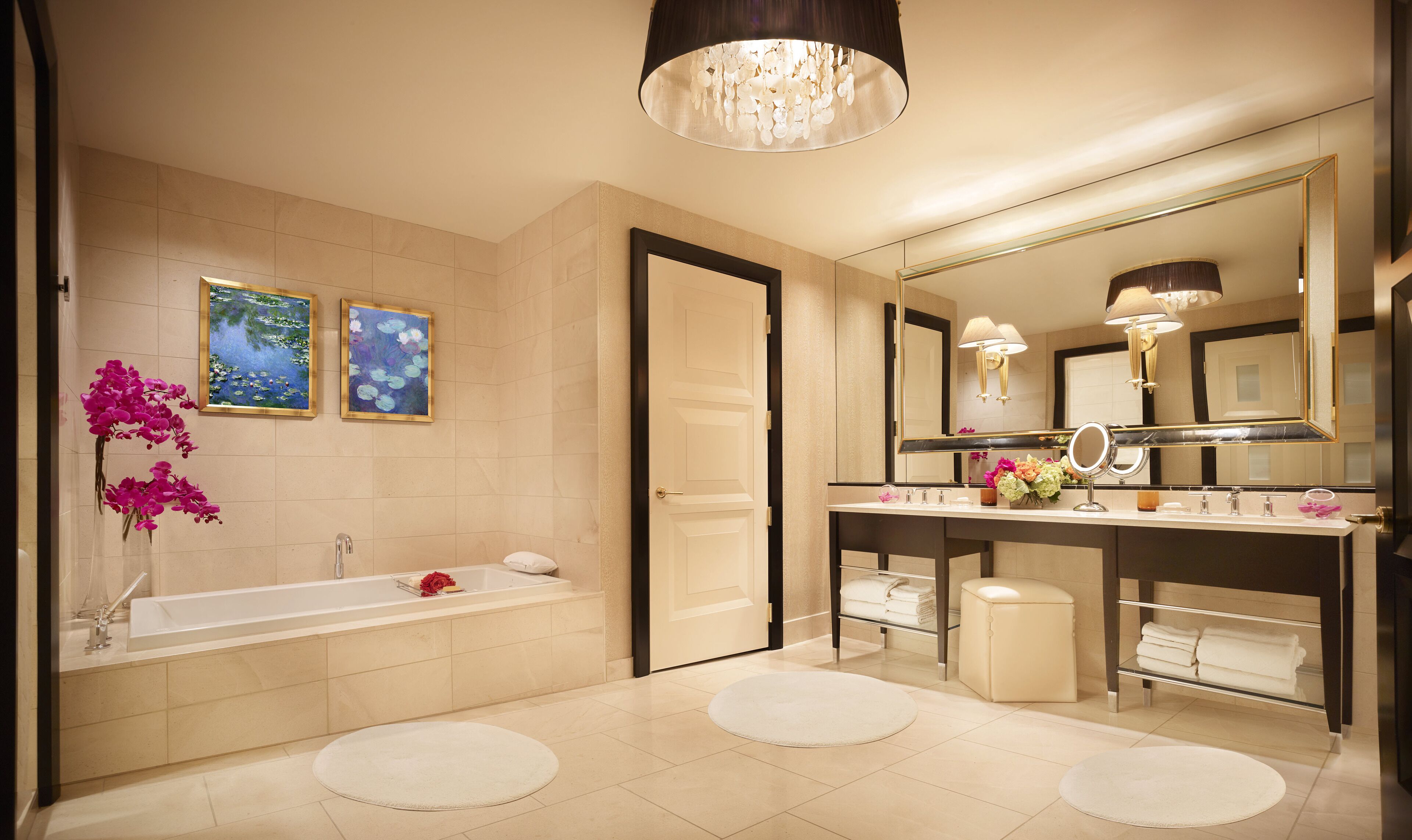 A modern bathroom with a bathtub, a large mirror, and two framed paintings on the wall.